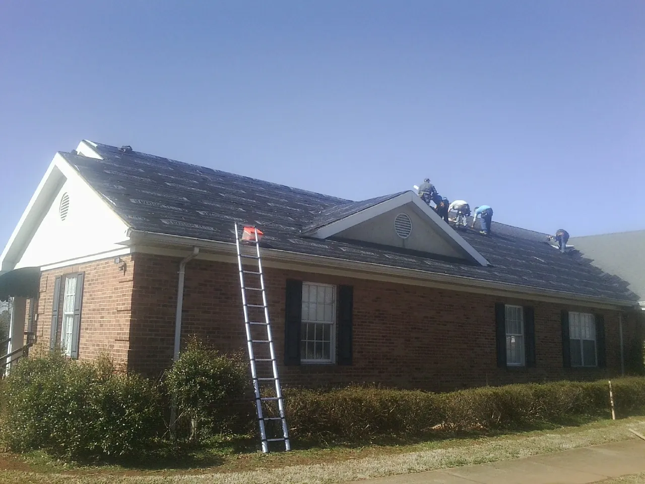 Crew tearing shingles off a brick ranch roof with a ladder set — Emergency Roof Repair work by our crew in Lincoln