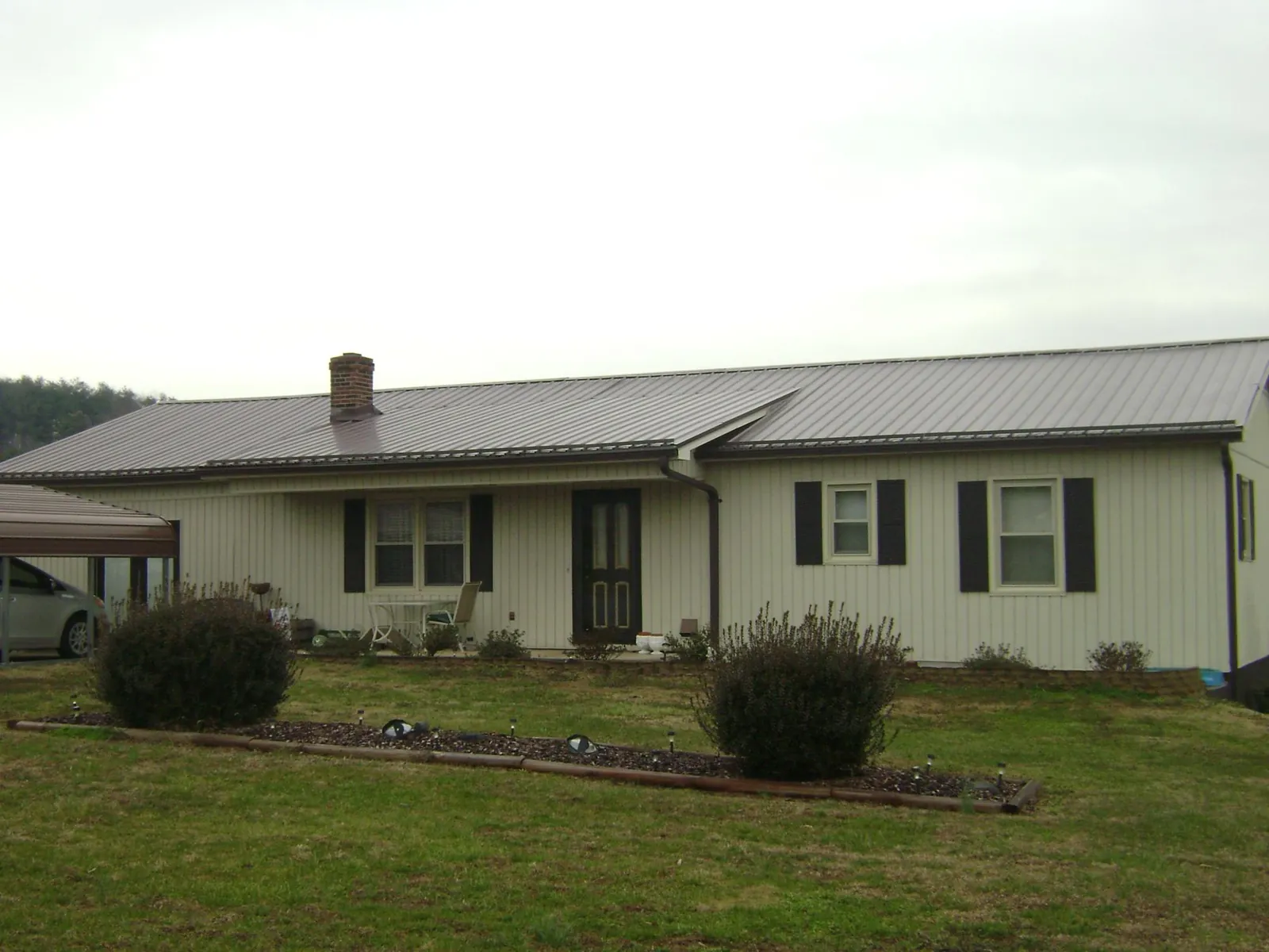 Brown metal roof on a cream sided ranch home with a brick chimney in Lincoln